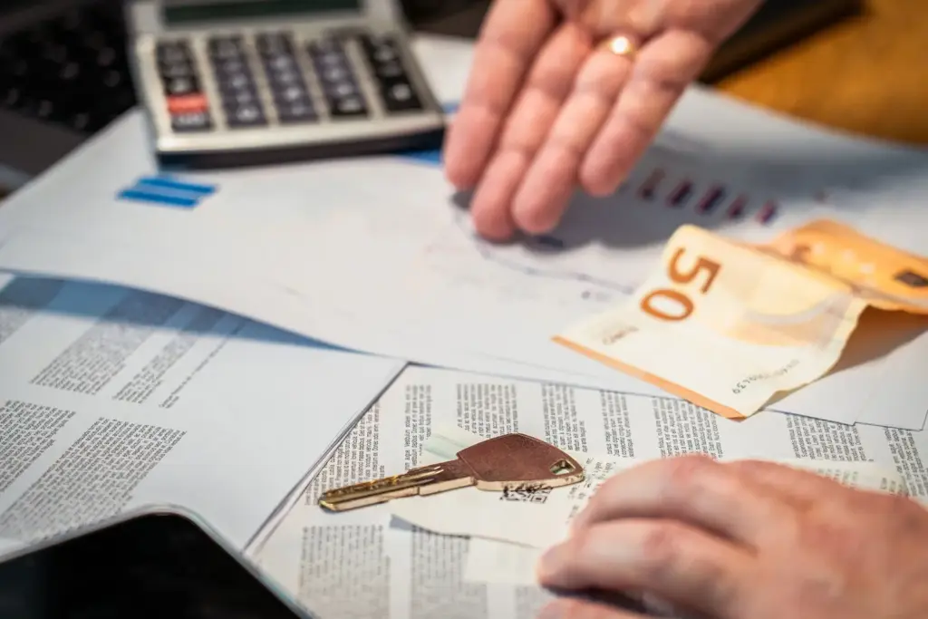 Hausschlüssel, Eurobanknote, Taschenrechner und Finanzunterlagen auf einem Tisch