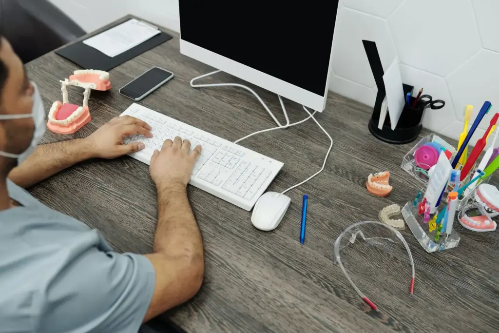 Zahnarzt arbeitet am Computer neben Zahnmodellen und Praxisinstrumenten