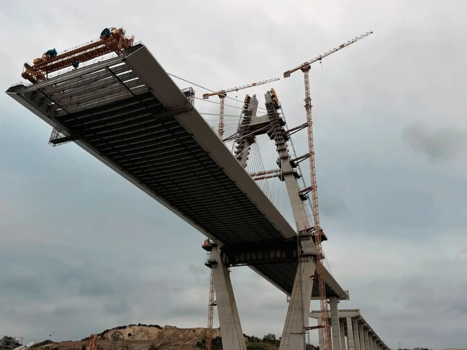 Unfertige Brücke mit mehreren Kränen auf einer großen Tiefbaustelle