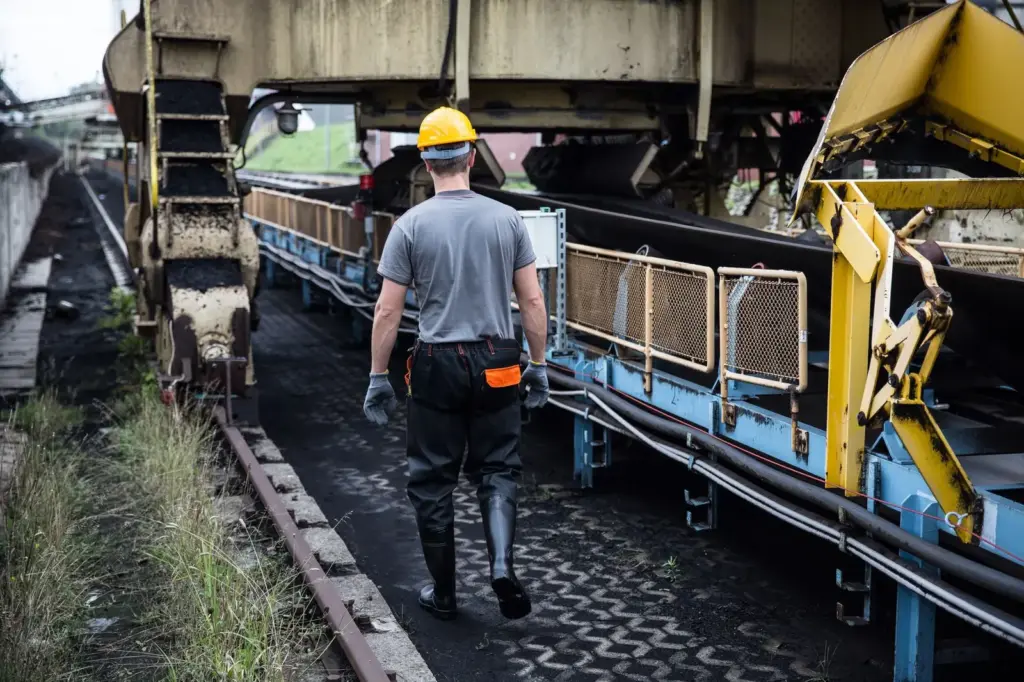 Arbeiter mit Schutzhelm und Handschuhen an einer industriellen Förderanlage
