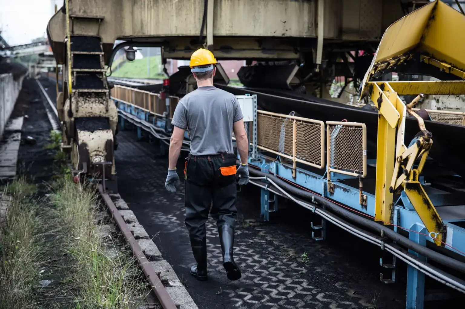 Arbeiter mit Schutzhelm und Handschuhen an einer industriellen Förderanlage