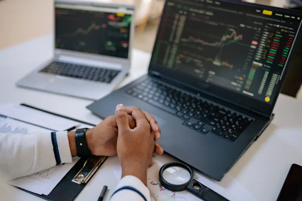 Hände vor zwei Laptops mit Kursdiagrammen und Finanzmarktdaten