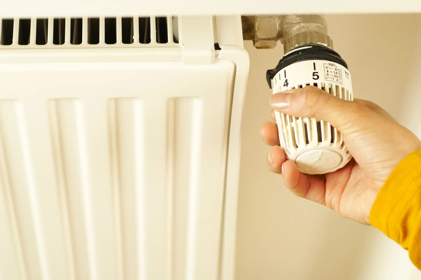 Hand stellt das Thermostatventil an einem Heizkörper ein