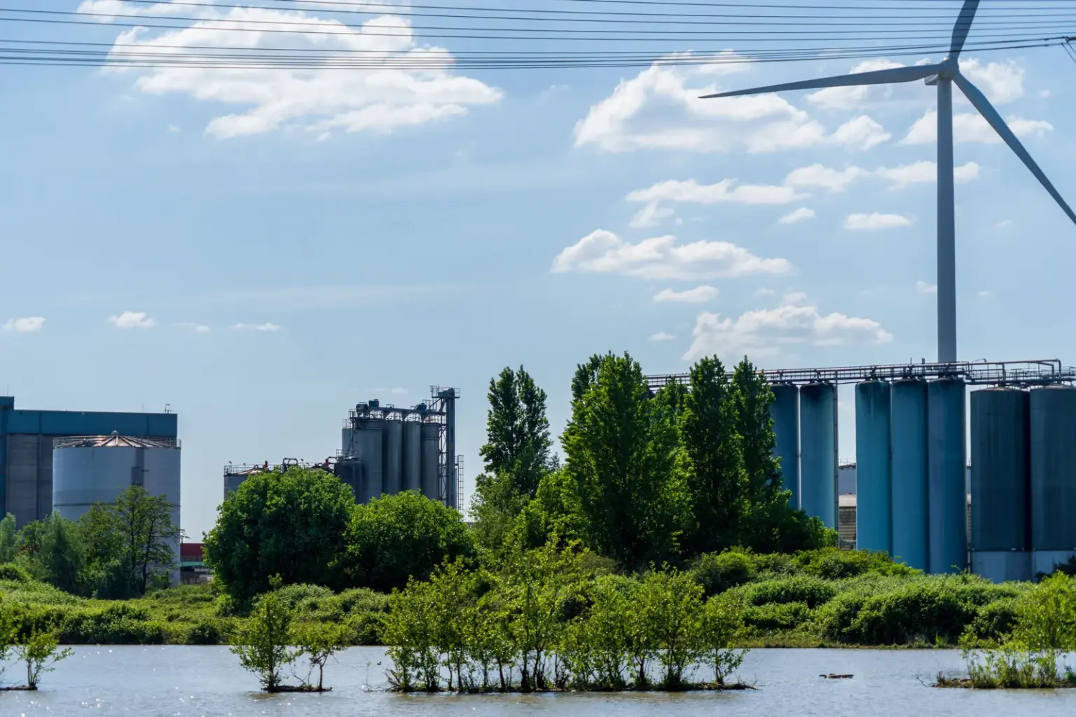 Industrieanlage mit Windkraftanlage und Stromleitungen an einem Fluss