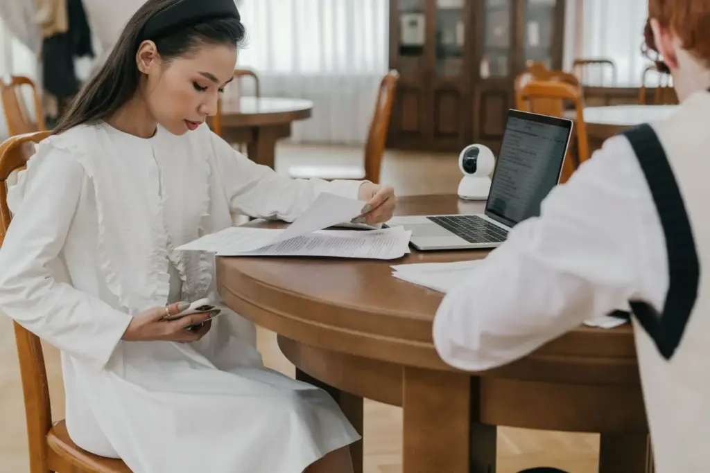 Zwei Studierende prüfen Finanzierungsunterlagen an einem Tisch mit Laptops