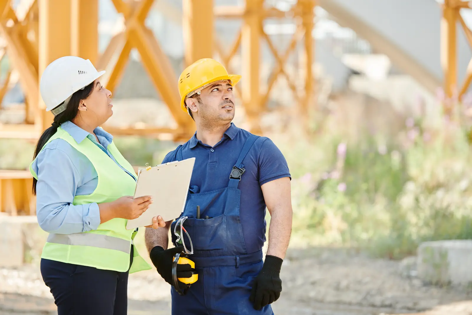 Zwei Fachkräfte mit Schutzhelmen besprechen Unterlagen auf einer Baustelle