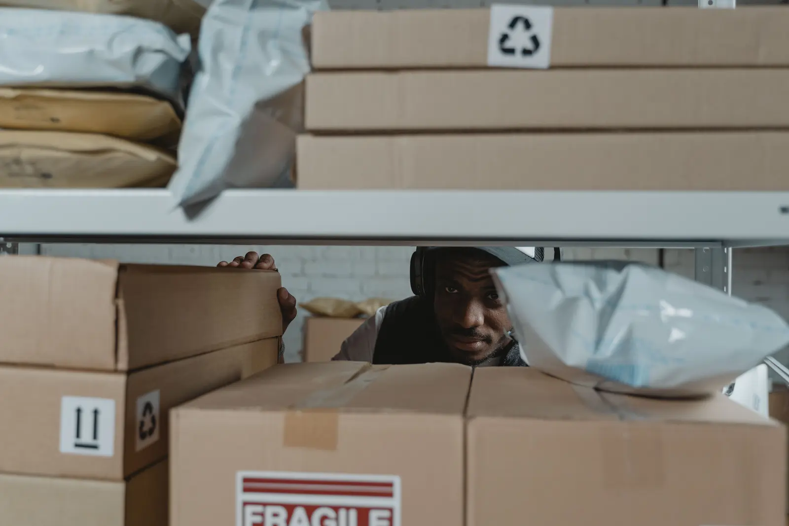 Mitarbeiter prüft Pakete zwischen gefüllten Regalen in einem Logistiklager