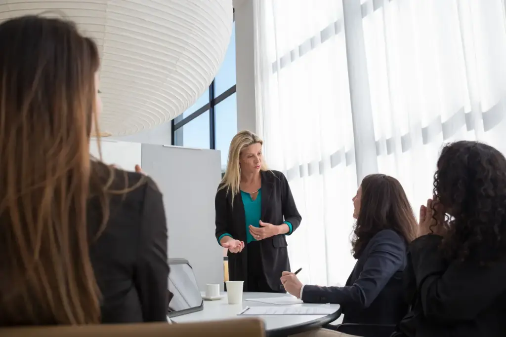 Frau leitet in einem hellen Büro eine Besprechung mit mehreren Kolleginnen