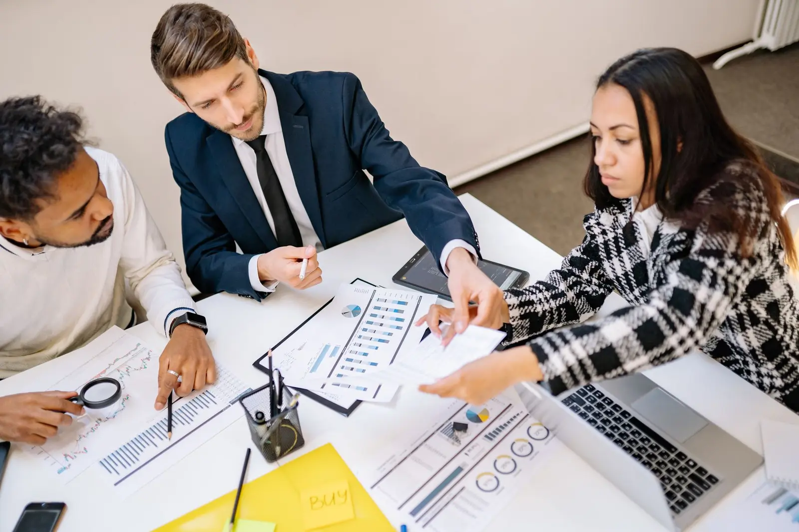 Drei Fachkräfte besprechen Diagramme und Wirtschaftsdaten an einem Bürotisch