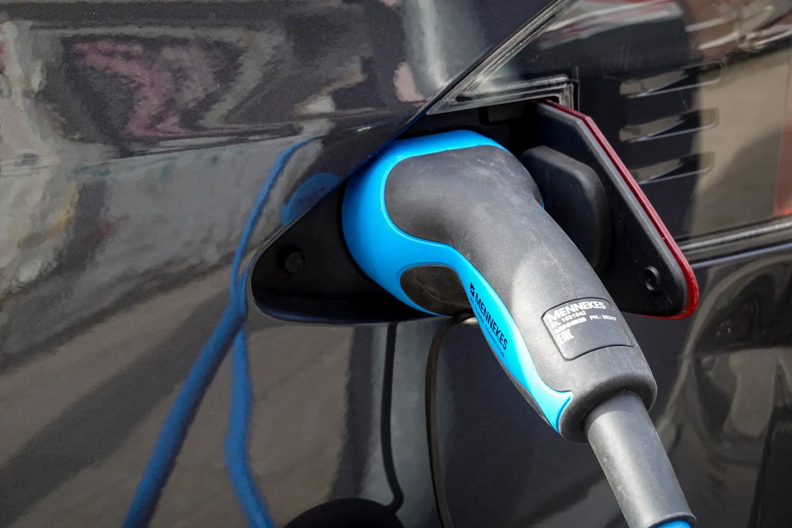 Blauer Ladestecker steckt im Ladeanschluss eines dunklen Elektroautos