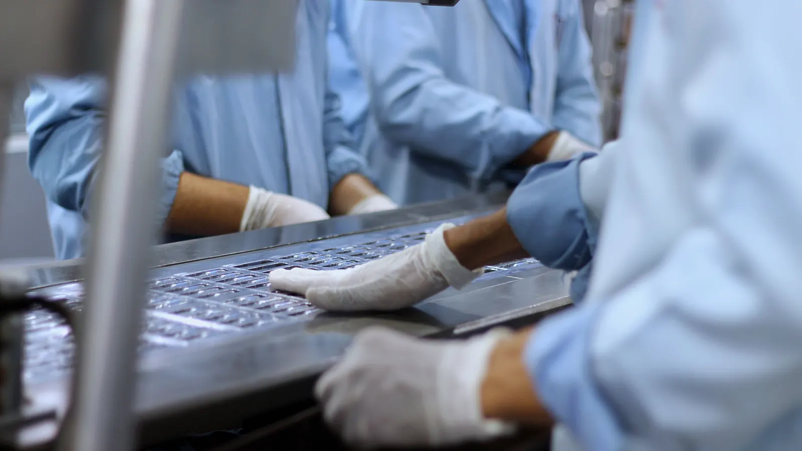 Beschäftigte mit Handschuhen kontrollieren Tablettenblister in einer pharmazeutischen Produktionsanlage